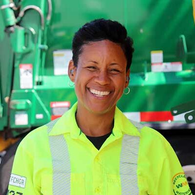 WM residential collections driver, Antoinette Flood, smiling in front of a green garbage truck