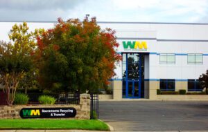 the front entrance to sacramento recycling transfer station with trees in the foreground and a building with the WM logo in the background