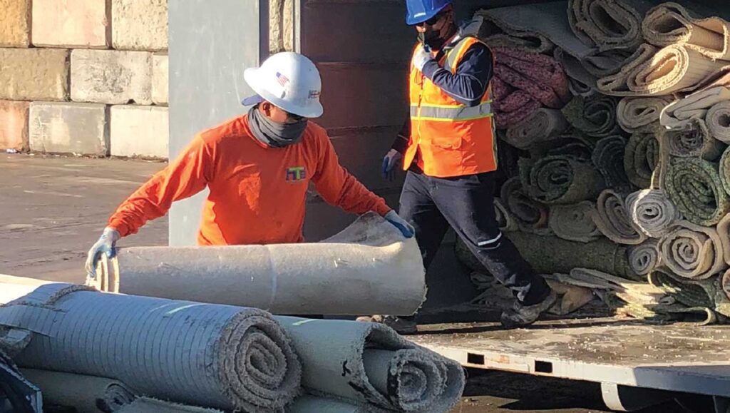 workers loading rolls of carpet onto a truck for recycling